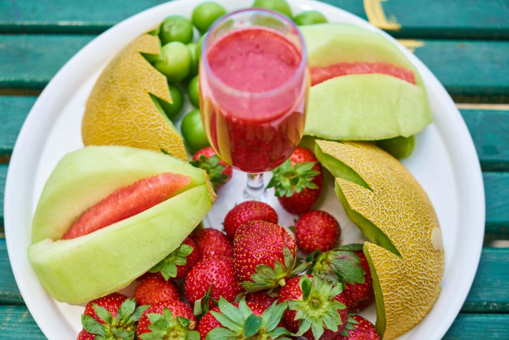 Refreshing platter of mixed fruits and strawberry juice on a white plate, offering a healthy and vibrant meal.