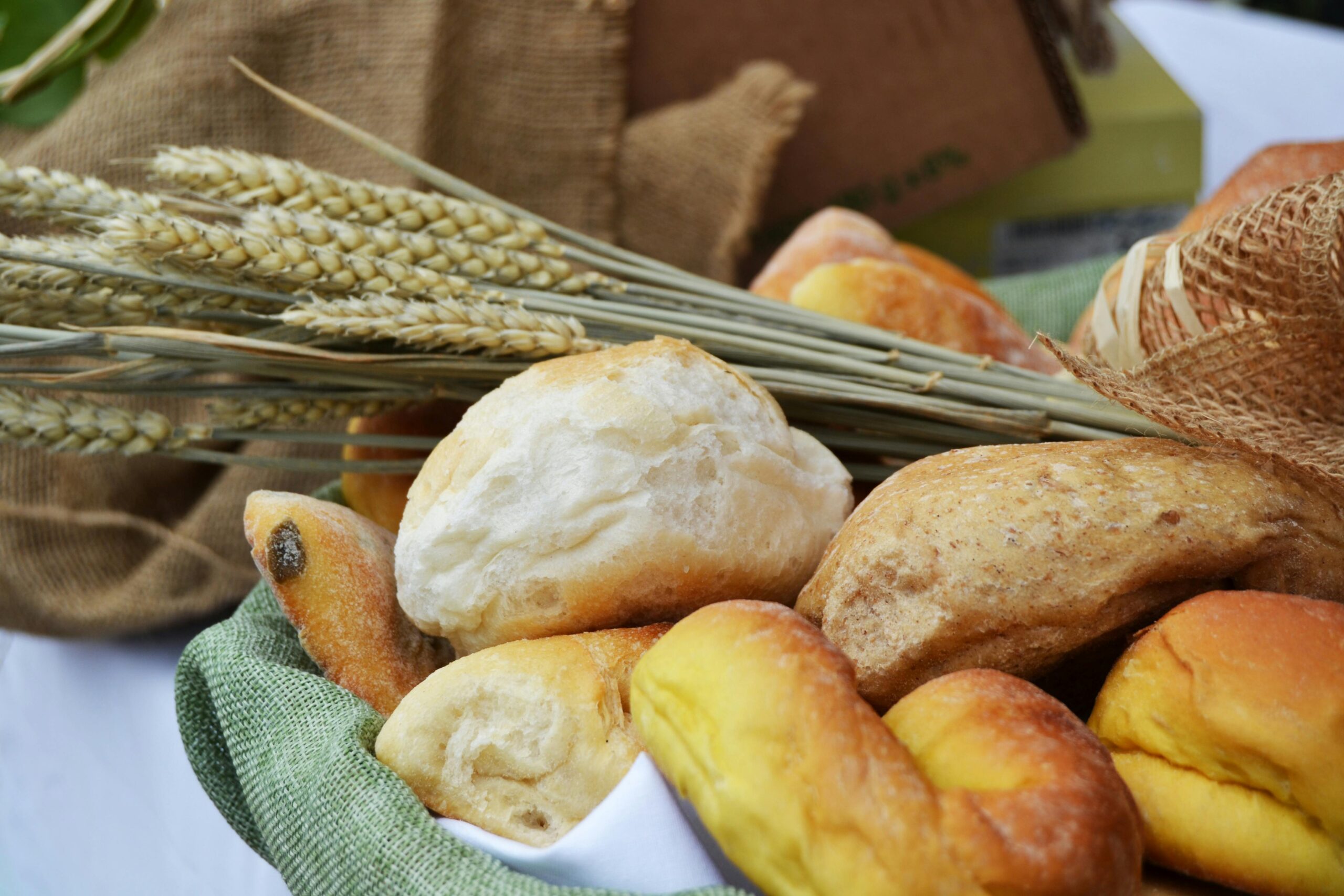 A variety of fresh breads in a basket surrounded by wheat stalks and rustic decor.