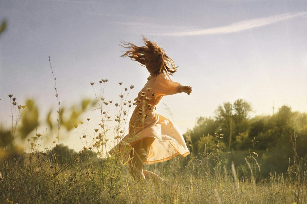 A carefree young woman in a dress dances joyfully in a sunlit meadow.